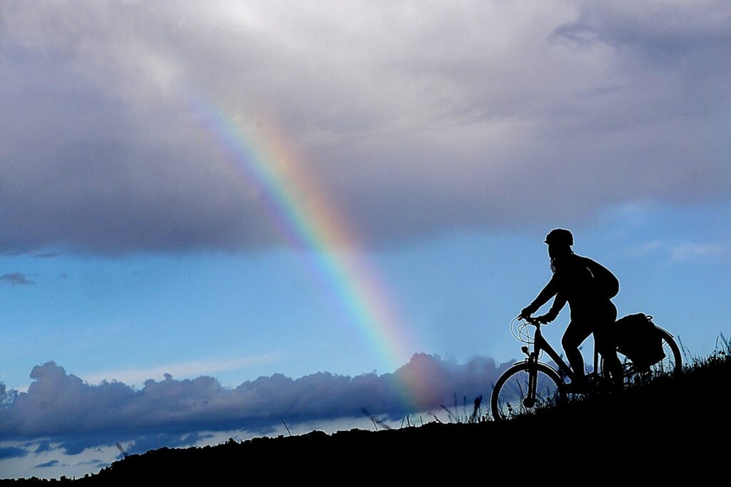 Cicloturista in controluce su un crinale con arcobaleno
