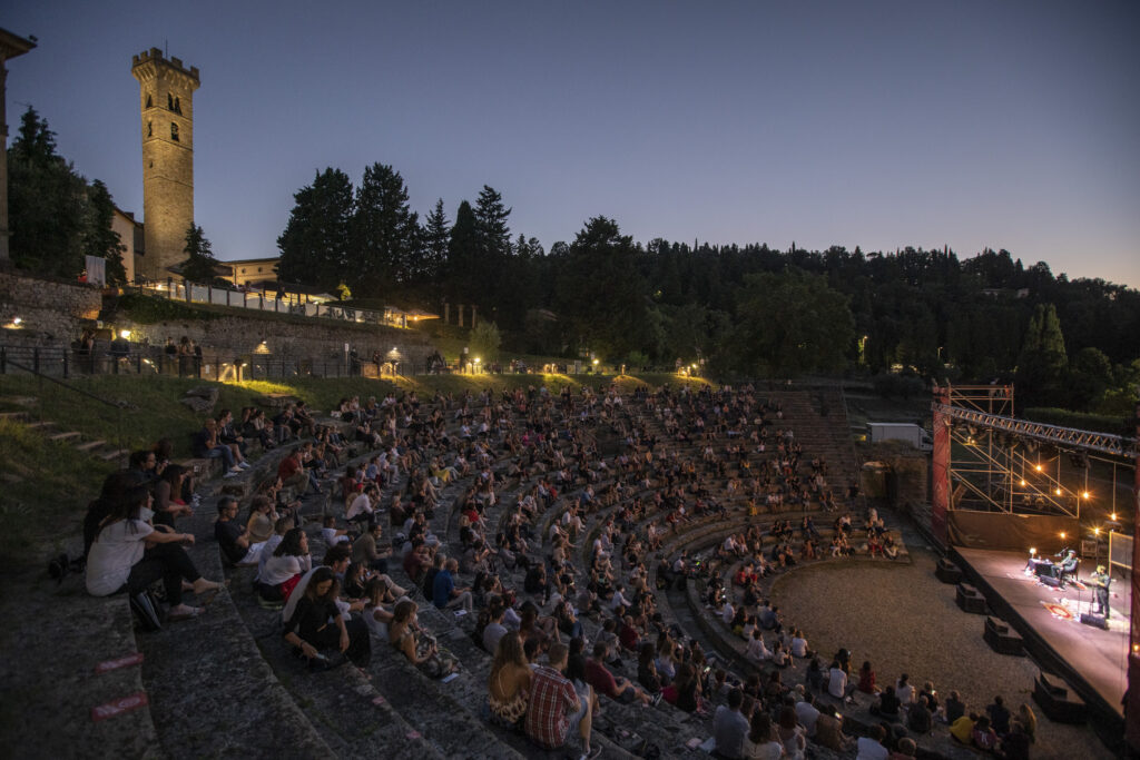 Pubblico sugli spalti del Teatro Romano di Fiesole durante un spettacolo in notturna