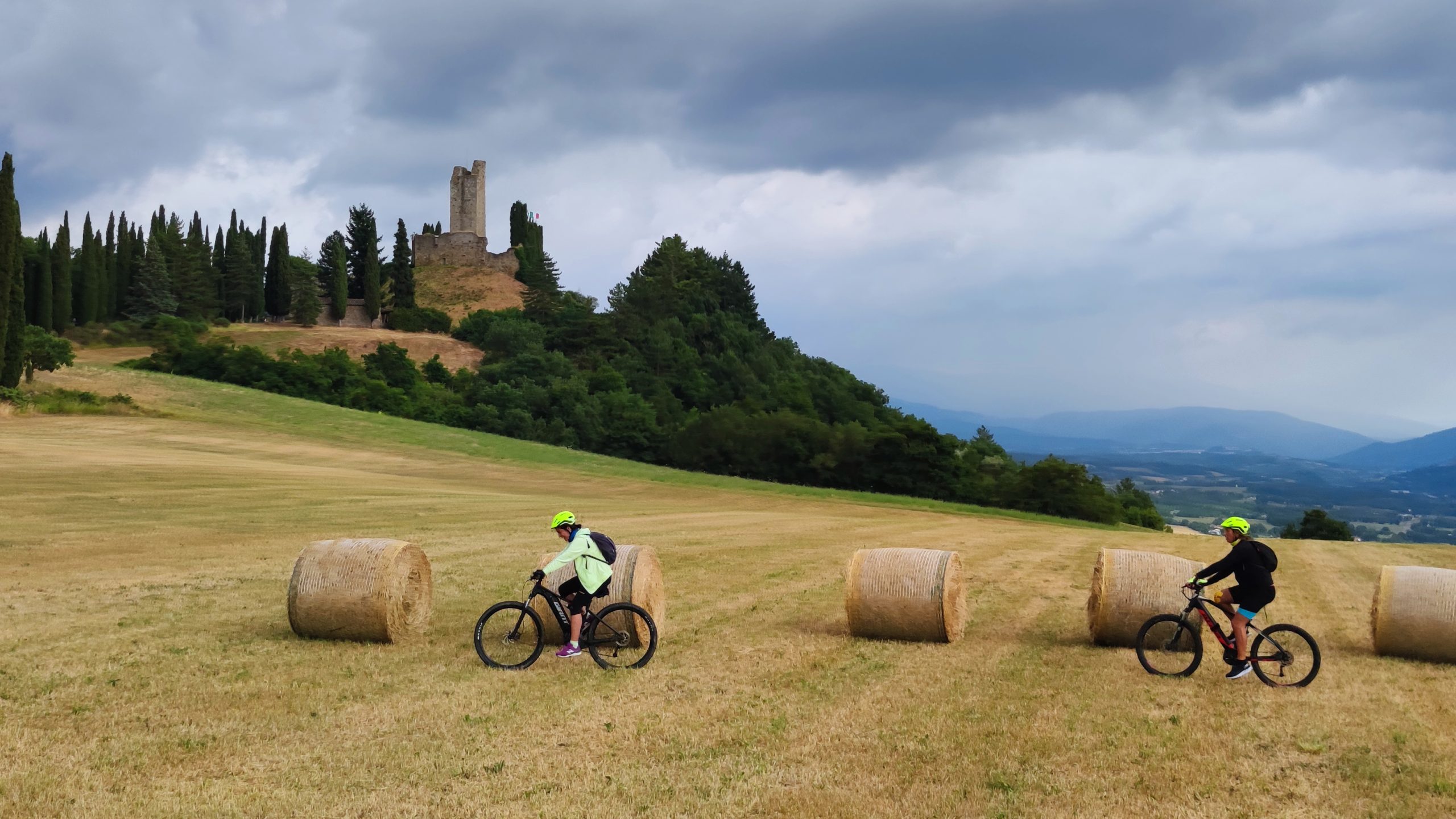 Romena Casentino pghoto by Riccardo Conti Nell'immagine, due persone che pedalano lungo un pendio erboso con una rocca alle loro spalle